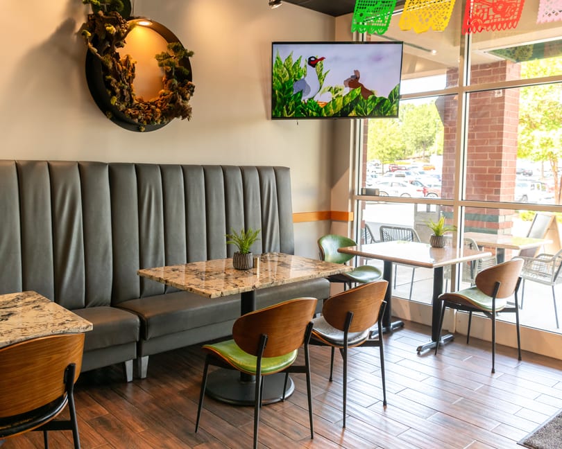 Restaurant interior with gray booth seating, marble tables, green chairs, and a TV showing cartoons.