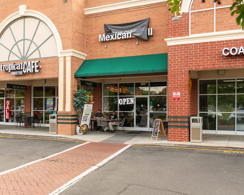 Exterior of a brick building with Tropical Cafe and Mexican restaurants, featuring outdoor seating and patrons.