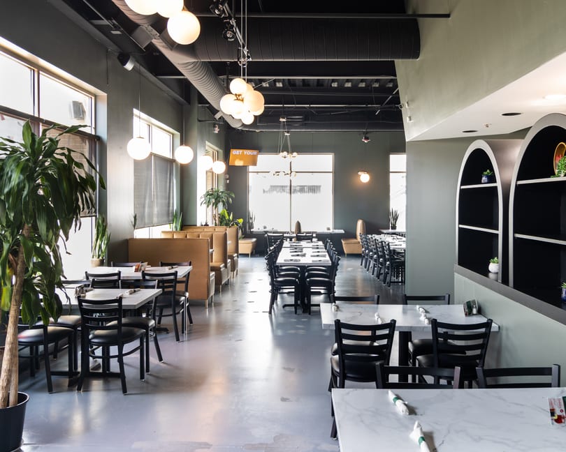 Spacious restaurant interior with marble-top tables, black chairs, booth seating, and modern globe lighting.