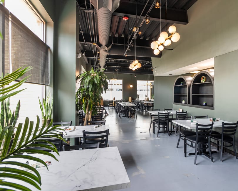 Spacious restaurant dining room with marble tables, black chairs, large windows, and green walls.