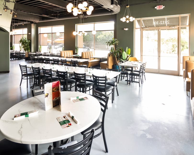 Spacious, modern restaurant interior with dark green walls, white marble tables, black chairs, and large windows.