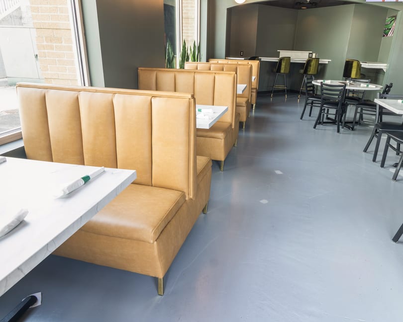 A modern restaurant interior with tan booths, white marble tables, and green walls.