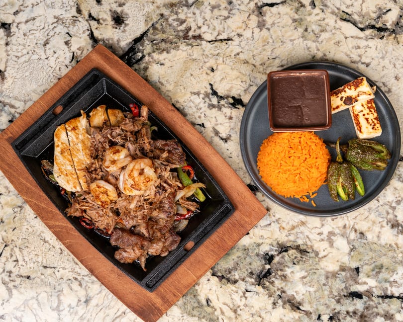 Sizzling fajita platter with chicken, shrimp, and beef, served with rice, beans, and grilled peppers.