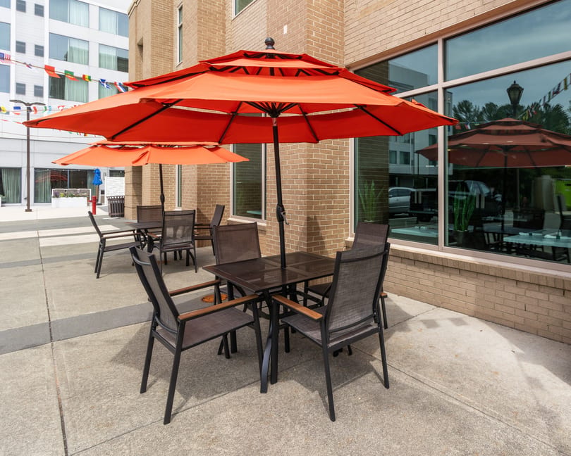 Outdoor patio with orange umbrellas, dark tables, and chairs next to a brick building.