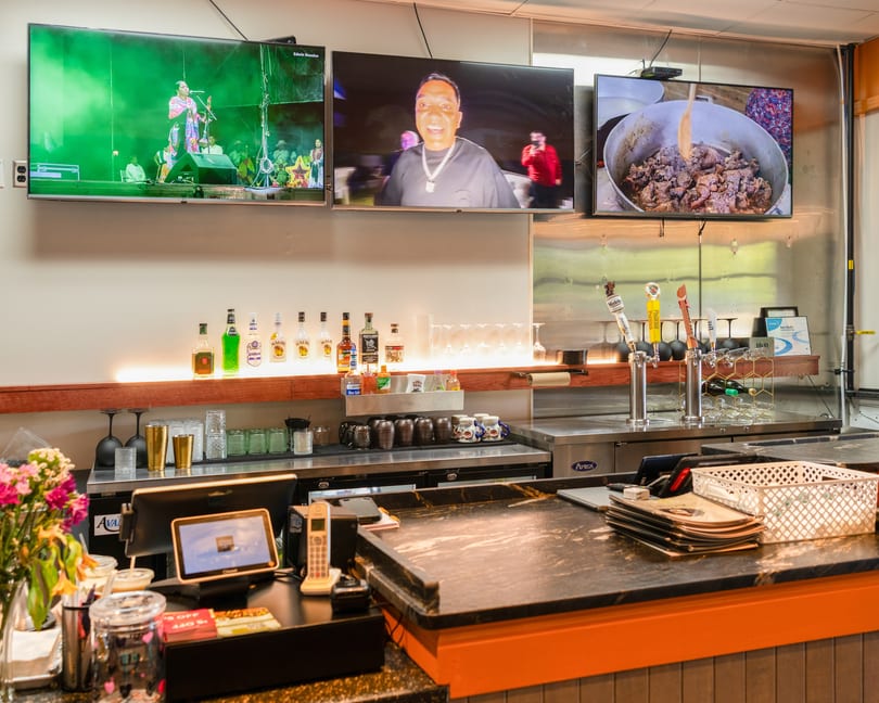 A restaurant bar with three TVs showing different programs, liquor bottles, beer taps, and barware.