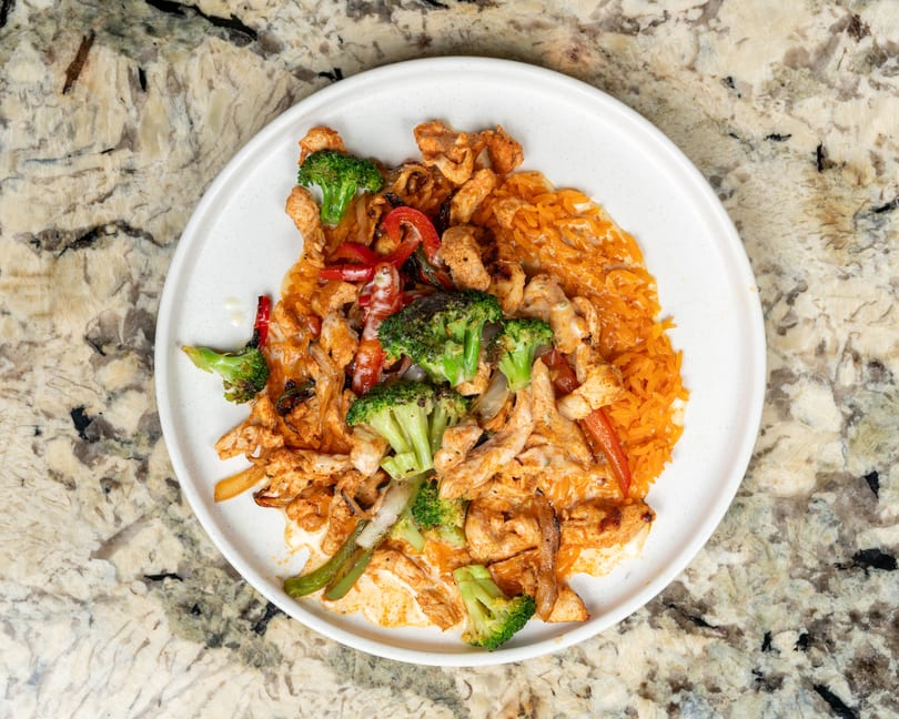 Chicken fajitas with broccoli, bell peppers, onions, and rice on a white plate.